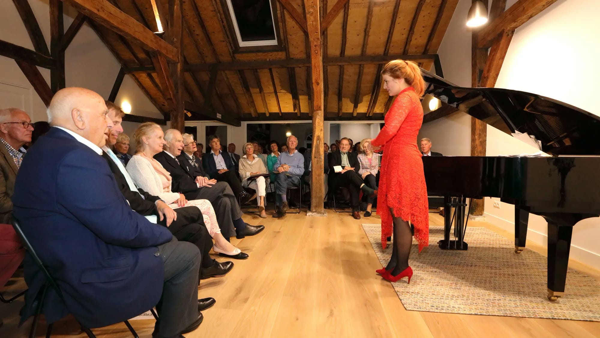 Zangeres in een rode jurk bij de vleugel, het publiek dichtbij onder de houten kap