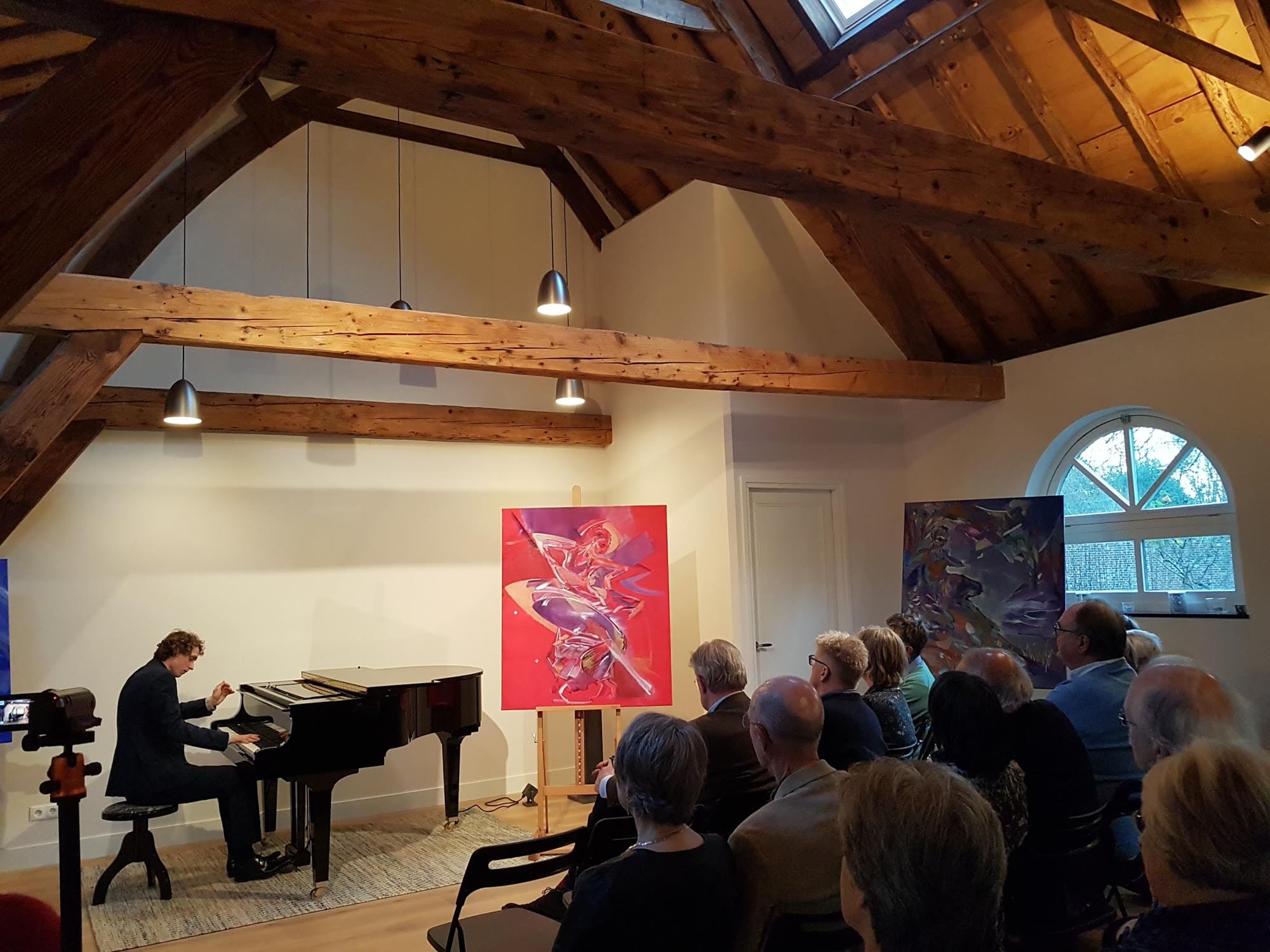 Pianist aan de vleugel tussen kleurrijke schilderijen, het publiek op de voorgrond